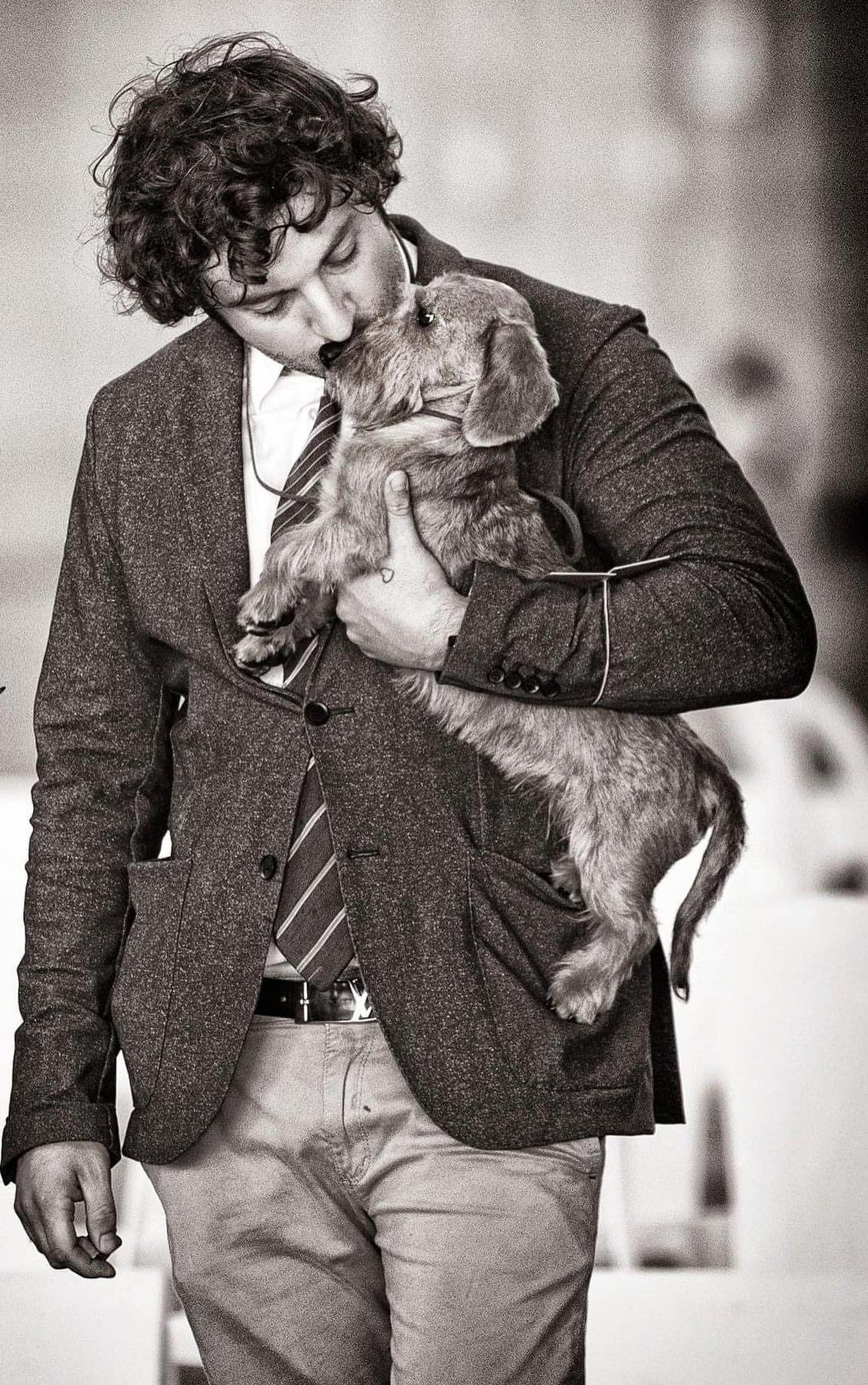 Black-and-white photograph: Gabriel in a tweed jacket kissing a young wirehaired dachshund held against his chest